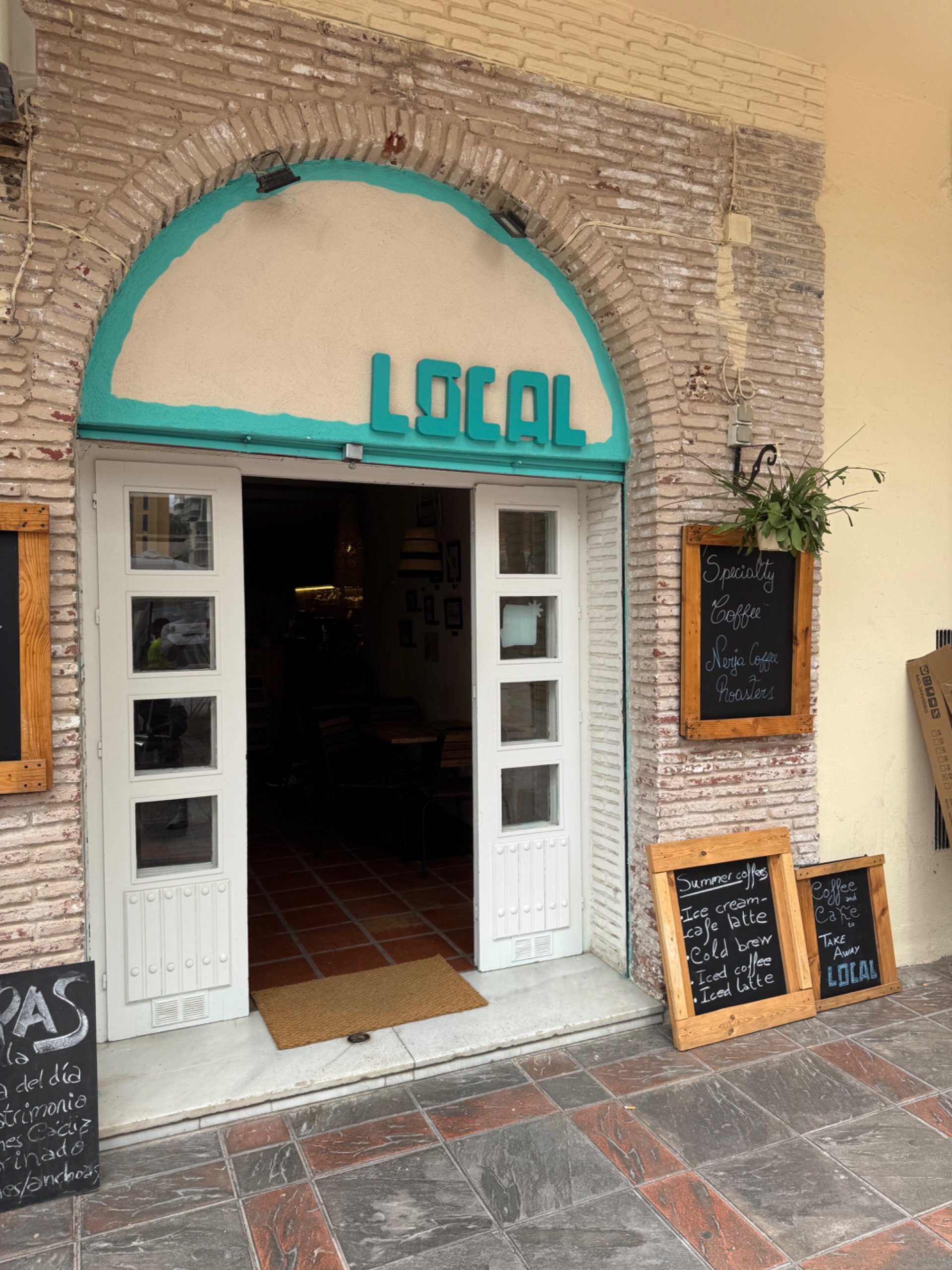 Ceglane wejście z napisem LOCAL i tablicą „Specialty coffee”